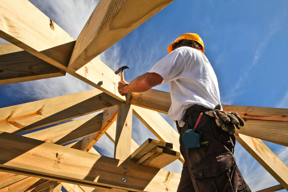 Zimmerer auf einer Dachkonstruktion Dachdecker/Zimmerer baut Holzgerüst für ein Dach, schlägt Nagel mit einem Hammer in Holzbalken